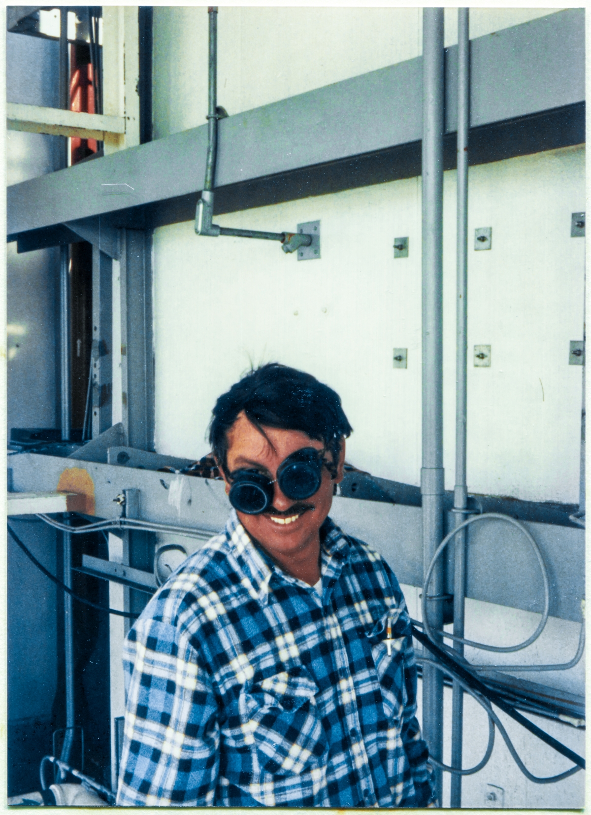 Image 065. Ironworker Gene Lockamy out of the Local 808 Union Hall working for Ivey's Steel Erectors at Space Shuttle Launch Complex 39-B, Kennedy Space Center, Florida, takes a momentary break from his work modifying the Rotating Service Structure in the area of the Girts which hold up the insulated metal paneling along the back side of the Payload Changeout Room, and unexpectedly pulls his cutting-torch goggles down at an absurd angle to laughingly oblige the photographer's request for an on-the-job photograph, up on high steel. Photograph by James MacLaren.